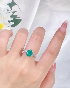Detailed view of an oval emerald gemstone ring with side diamonds on model's hand