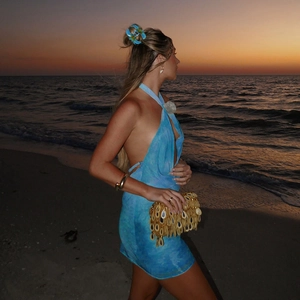 Blue halter backless mini dress with shell clutch bag at sunset beach vacation scene