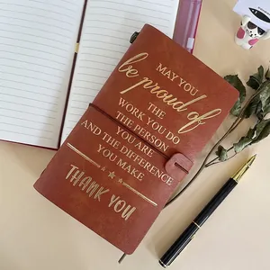 Brown faux leather notebook with gold foil lettering and elastic closure on warm background