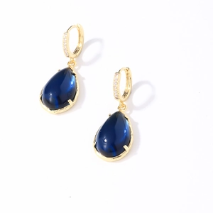 Macro detail of gold earrings with teardrop blue gemstone and sparkling zircons