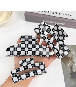 Detail of three black and white checkered hair claws held by hand with a book background