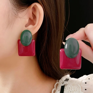 Close-up of resin earrings featuring green oval and pink square geometric drops