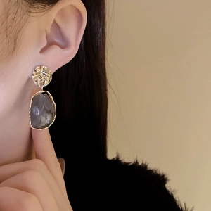 Close-up of model wearing irregular grey resin earrings with vintage gold metal accents