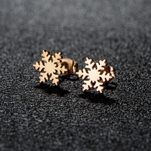 Minimalist gold snowflake stud earrings for women on a textured black background