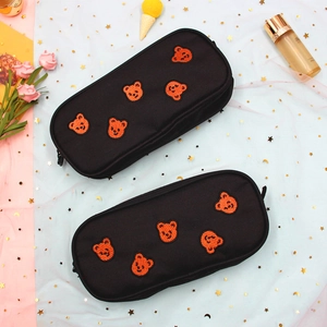 Detailed embroidery of orange bear heads on black canvas pencil cases with gold zippers