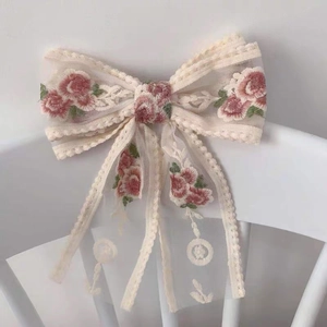 Detail of ivory lace hair bow with pink floral embroidery and elegant long streamers