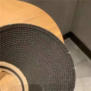 Detailed close-up of woven black straw sun hat with beige decorative trim on the edge