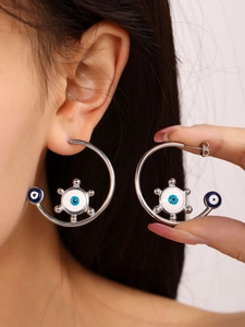 Detail of silver C-hoop earrings with enamel evil eye charms on female model