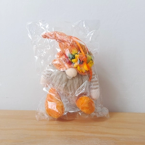 Close-up of a plush Thanksgiving gnome with orange knit hat and sunflower in poly bag