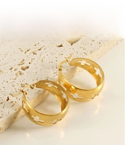 Macro shot of gold stainless steel hoop earrings with hollow cross patterns on stone pedestal