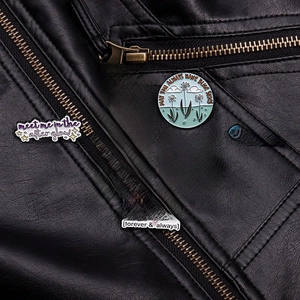 Detail of colorful enamel pins with music quotes pinned on a black leather jacket texture