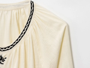Gros plan sur la broderie du col en V et la texture lin d'une chemise beige rétro