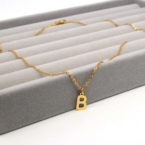Detailed view of golden stainless steel necklace with letter B pendant on velvet tray