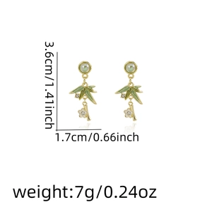 Detail shot of green bamboo leaf earrings with gold branches and white flowers