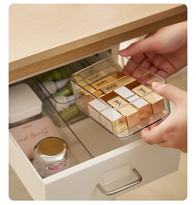 Hand placing a transparent plastic drawer organizer filled with lipstick into a white drawer