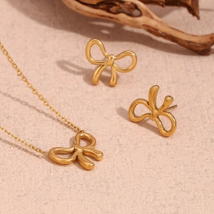 Close-up of golden bow-shaped necklace and stud earrings set on a natural background