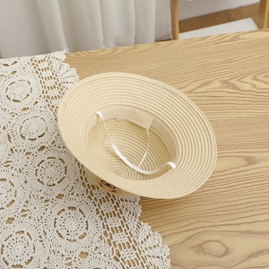 Detail of light beige woven straw hat with cute bear embroidery and elastic wind strap