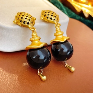 Detailed close-up of vintage gold woven texture earrings with black spherical drops