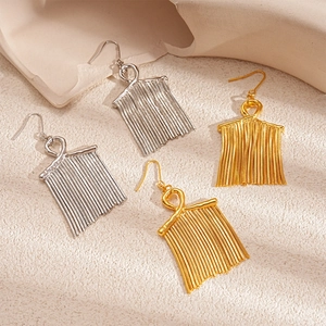 Elegant gold and silver tassel earrings with artistic knotted design on stone background