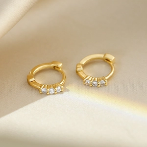 Macro view of gold hoop earrings with three inlaid sparkling round zircons on silk