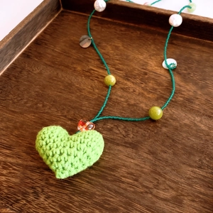 Détail d'un pendentif cœur au crochet vert fait main avec perles sur plateau bois