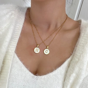 Detail of layered gold stainless steel necklaces with H and C initial round pendants