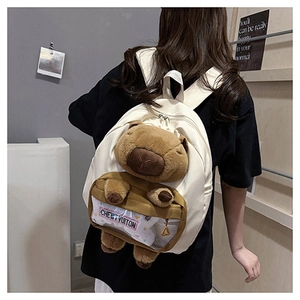 White canvas backpack detail with 3D capybara plush toy and clear PVC pocket window