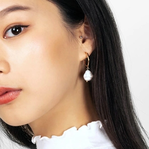 Close-up of irregular baroque pearl drop earrings in gold finish on a female model
