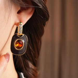 Close-up of vintage gold-framed black rectangular earring with amber gemstone