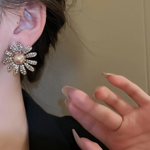 Detailed close-up of golden floral earring featuring central pearl and sparkling rhinestones