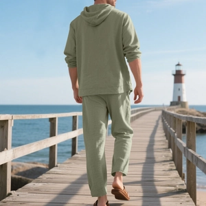 Men's sage green linen blend hooded shirt and trousers set walking on a beach boardwalk
