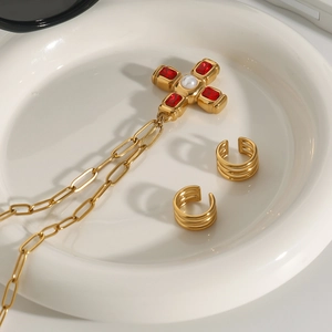 Détail du collier croix dorée avec rubis rouges et perles sur une assiette blanche