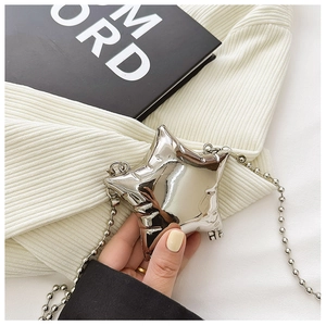 Macro shot of a shiny silver star-shaped metal mini bag with ball chain on textured fabric