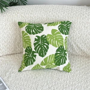 Detail of green monstera leaf pattern on linen pillowcase against a white boucle sofa
