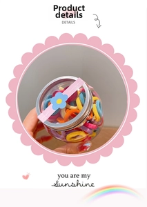 Close-up of colorful elastic hair bands stored in a clear jar with a pink wave border