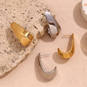 Close-up of hollow curved gold and silver plated earrings on a stone textured surface