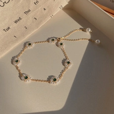Detail of flower bracelet with green stones and pearls on an elegant beige surface