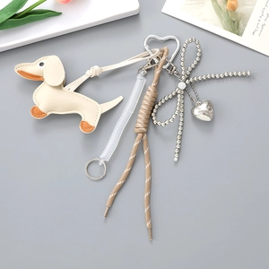 Detail of beige leather dachshund bag charm with heart buckle and beaded bow accessory