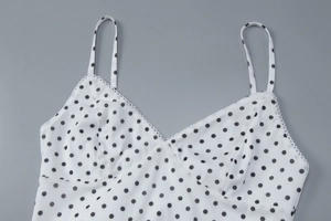 Close-up of white mesh fabric with black polka dots and delicate lace trim on the V-neckline