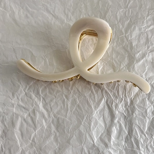 Close-up of a white cream-colored heart-shaped hair claw clip with gold metal spring detail
