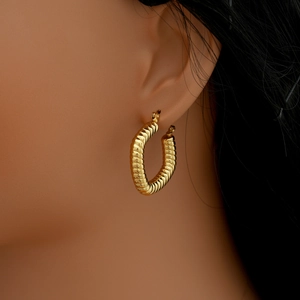 Gros plan d'une boucle d'oreille dorée torsadée en U portée par un mannequin avec éclat