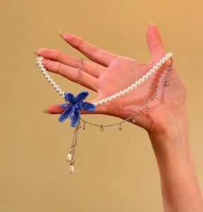 Elegant handmade blue beaded flower pearl necklace shown held in a hand for detail view