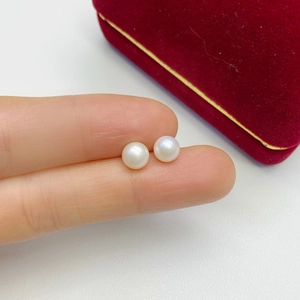 Detailed close-up of 6-8mm white freshwater pearl studs held for scale with a red jewelry box