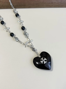 Macro detail of gothic black heart pendant with silver cross on beaded stone chain