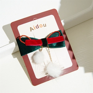 Detail of Christmas bow hair clip with velvet ribbons, gold chain, and white pom-poms