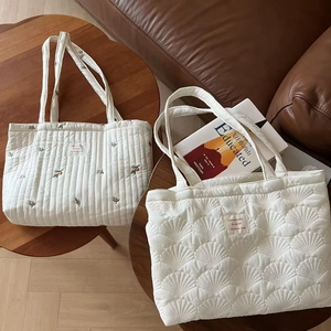Detailed view of quilted tote bag with floral embroidery and shell stitching texture