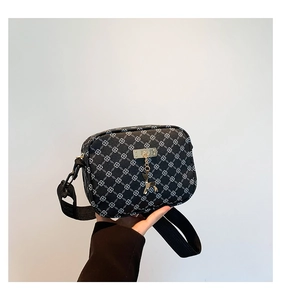 Detail of monogram shoulder bag featuring golden deer pendant and wide fabric strap