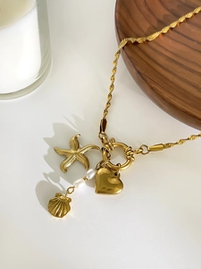 Detail of gold starfish, heart pendants and white pearls on a titanium steel necklace