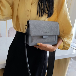 Grey flap square bag with suede patchwork and adjustable strap held by a model