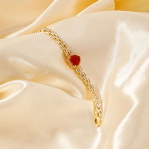 Detail of gold heart bracelet with ruby-colored stone and rows of clear zircons